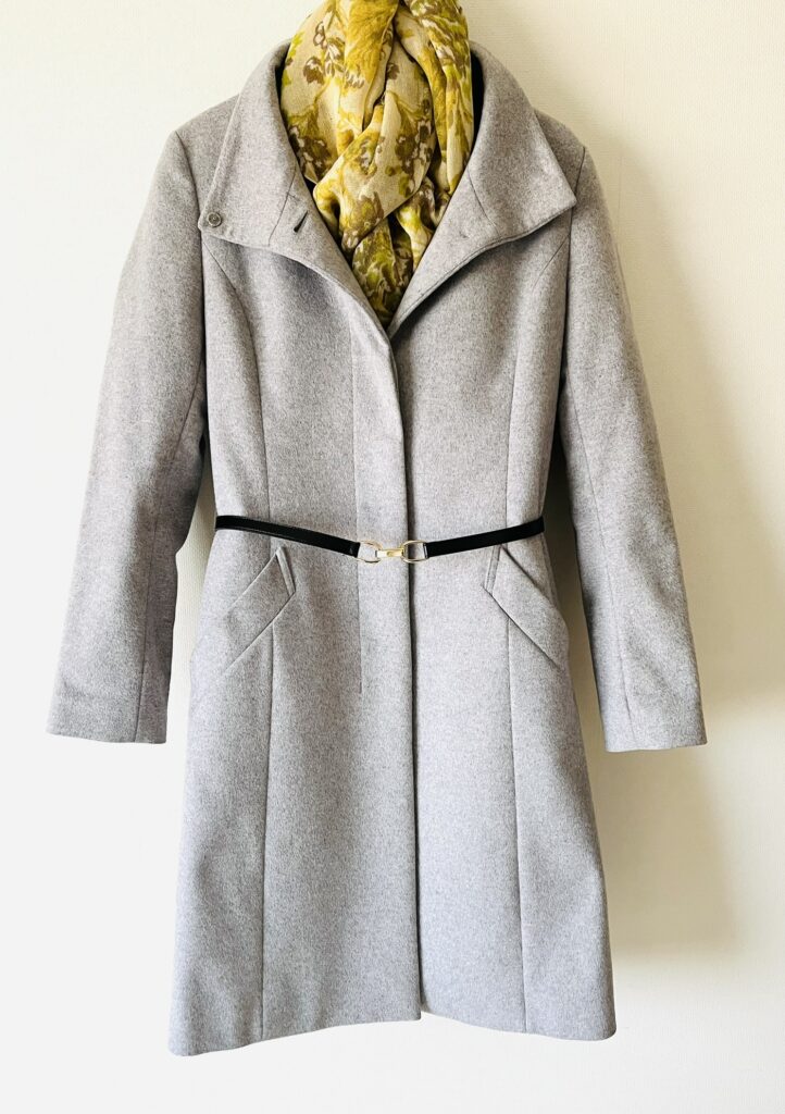ライトグレーのウールコートの40代向けコーデ。黄色のストールと黒革のベルトを追加。毛玉やよごれは目立ちにくいので、寿命が長い。お手入れも簡単。