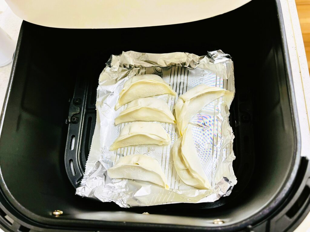 コストコ餃子計画の冷凍餃子のアレンジレシピ。ノンフライヤーでパリパリ餃子を作成中。庫内にホイルを敷いてから餃子をのせるとくっつかないので便利。